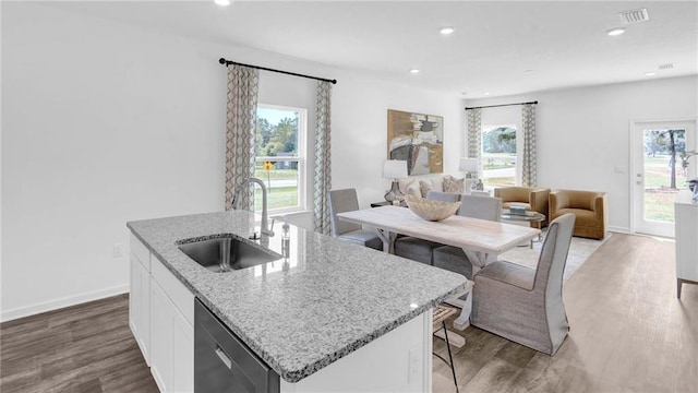kitchen featuring dishwasher, a sink, wood finished floors, a kitchen island with sink, and light stone counters