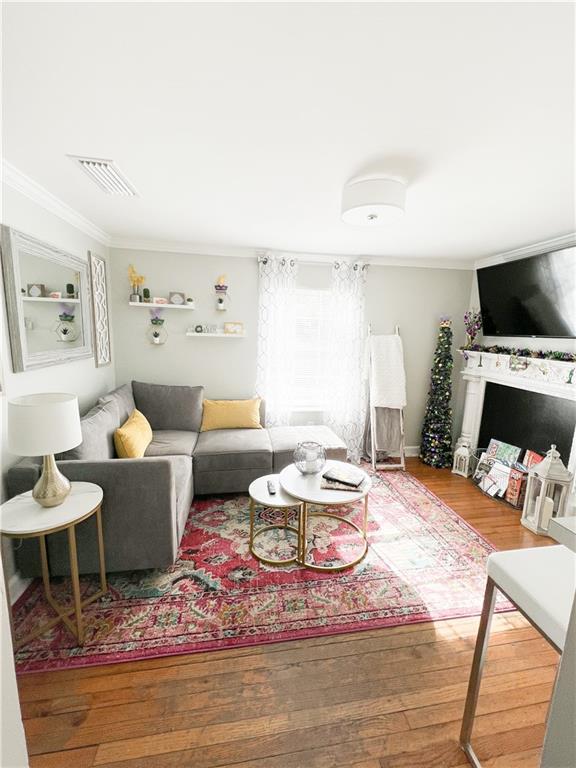 living area with visible vents, crown molding, and wood finished floors