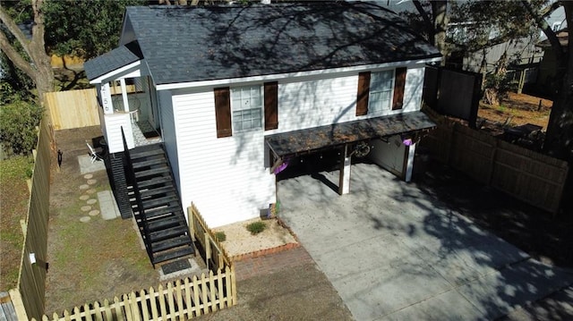 view of front of house with stairs, concrete driveway, fence, and roof with shingles