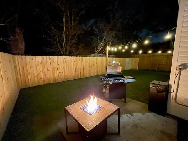 patio at night with a yard, a fire pit, and a fenced backyard