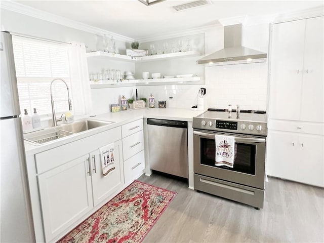 kitchen with visible vents, a sink, stainless steel appliances, crown molding, and wall chimney range hood