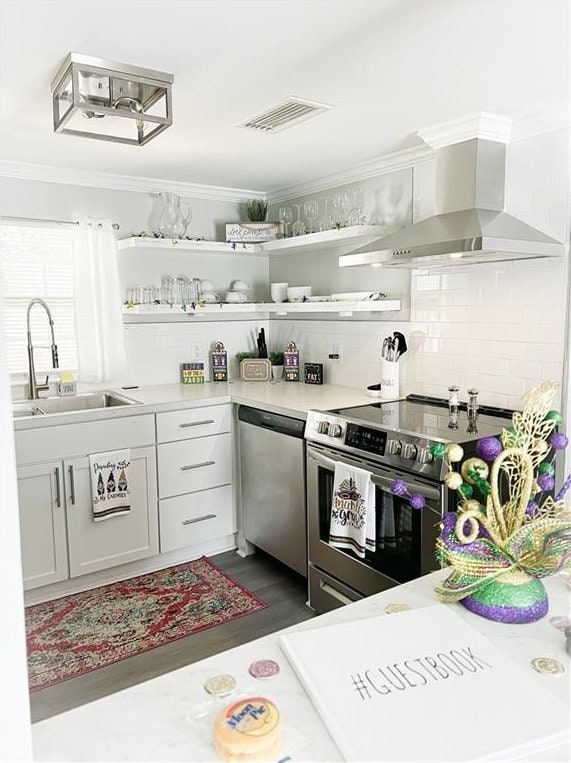 kitchen with visible vents, ornamental molding, a sink, appliances with stainless steel finishes, and wall chimney exhaust hood