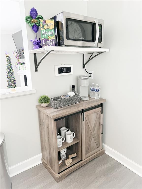 bar with light wood-type flooring, stainless steel microwave, and baseboards