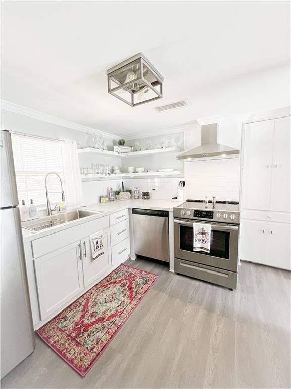 kitchen featuring open shelves, a sink, stainless steel appliances, crown molding, and wall chimney range hood