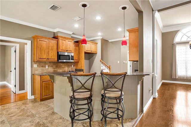 3245 Mcrae Dr, Mobile, AL 36695 - kitchen with stainless steel microwave, a kitchen breakfast bar, crown molding, decorative backsplash, and a peninsula