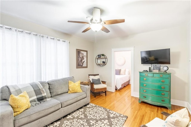 living area featuring a ceiling fan, light wood-style flooring, and baseboards
