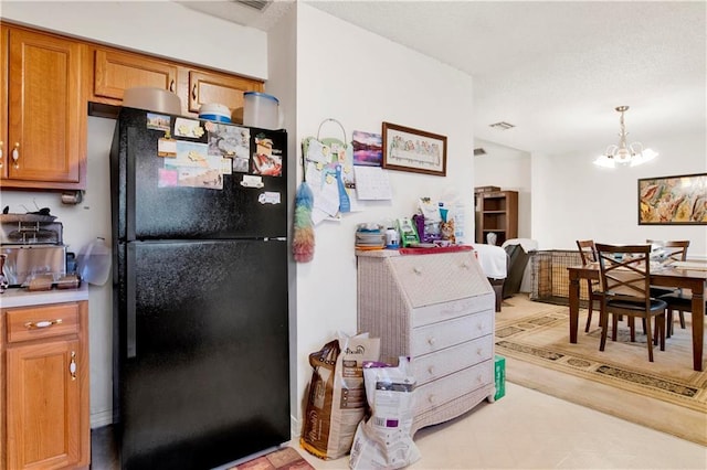 kitchen with freestanding refrigerator, light countertops, decorative light fixtures, a notable chandelier, and brown cabinets