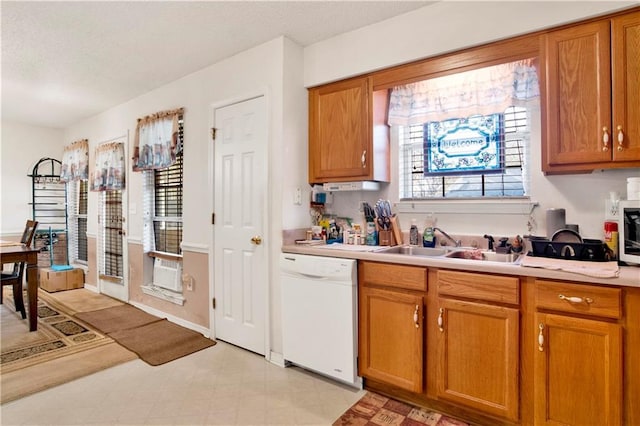 kitchen featuring a sink, brown cabinetry, white dishwasher, light floors, and light countertops