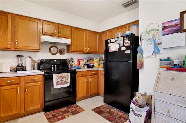 kitchen featuring visible vents, under cabinet range hood, light countertops, brown cabinets, and black appliances