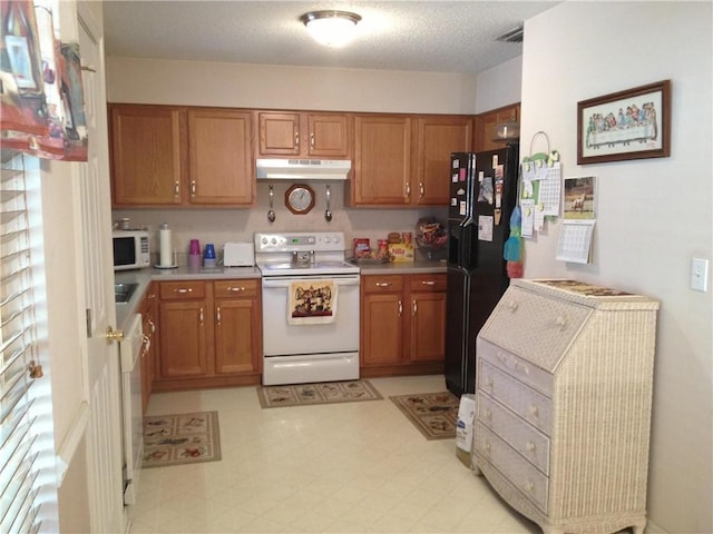 kitchen featuring under cabinet range hood, white appliances, light floors, and brown cabinets