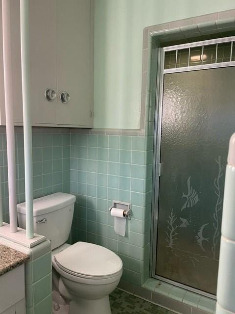 bathroom featuring vanity, toilet, a shower with door, and tile walls