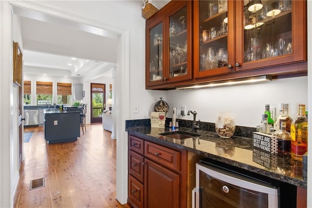 bar with beverage cooler, sink, light hardwood / wood-style flooring, dark stone countertops, and dishwasher