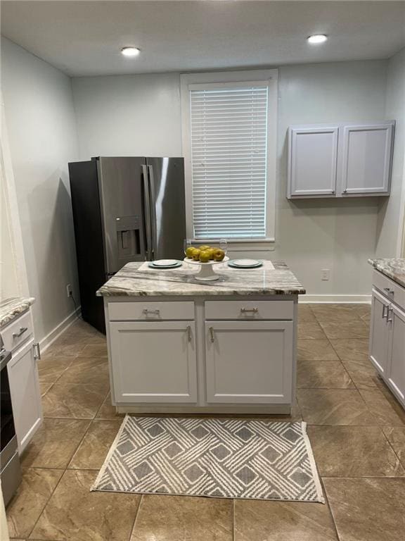 kitchen with light stone counters, stainless steel refrigerator with ice dispenser, and a kitchen island