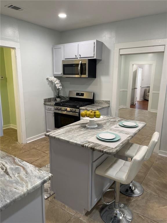 kitchen featuring appliances with stainless steel finishes, light tile patterned flooring, white cabinetry, light stone countertops, and a breakfast bar area