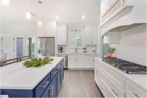 kitchen featuring white cabinets, blue cabinetry, appliances with stainless steel finishes, tasteful backsplash, and custom range hood