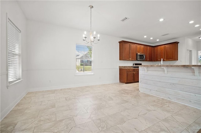 kitchen with kitchen peninsula, pendant lighting, light stone counters, a breakfast bar area, and a chandelier