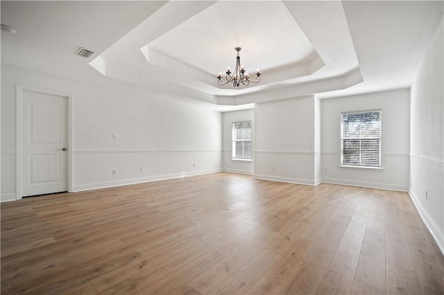 spare room with an inviting chandelier, a raised ceiling, light hardwood / wood-style floors, and plenty of natural light