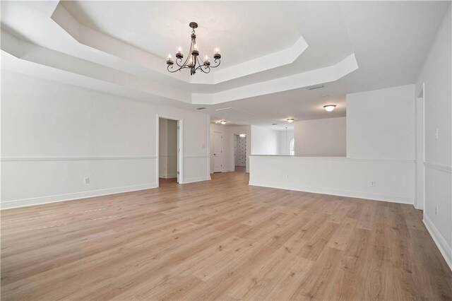 unfurnished room with a notable chandelier, a tray ceiling, and light wood-type flooring