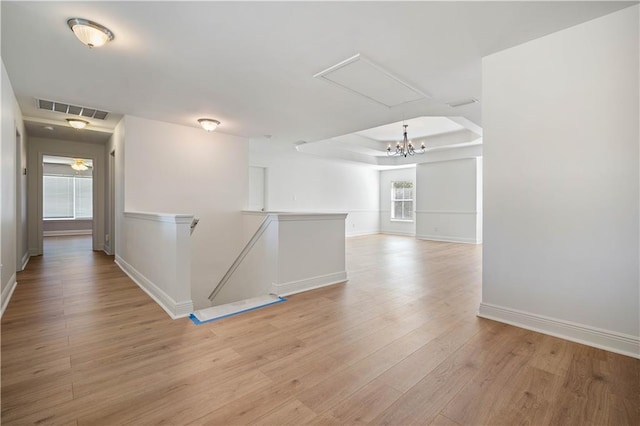 corridor featuring a notable chandelier, a tray ceiling, light hardwood / wood-style flooring, and plenty of natural light