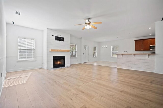 unfurnished living room featuring light hardwood / wood-style floors, sink, a large fireplace, and ceiling fan with notable chandelier