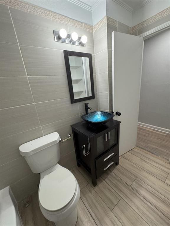 bathroom with crown molding, toilet, vanity, an inviting chandelier, and tile walls