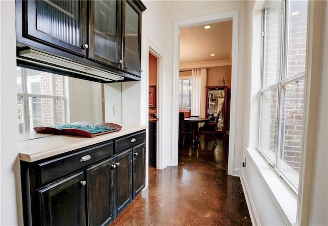 kitchen with finished concrete flooring, baseboards, ornamental molding, light countertops, and glass insert cabinets