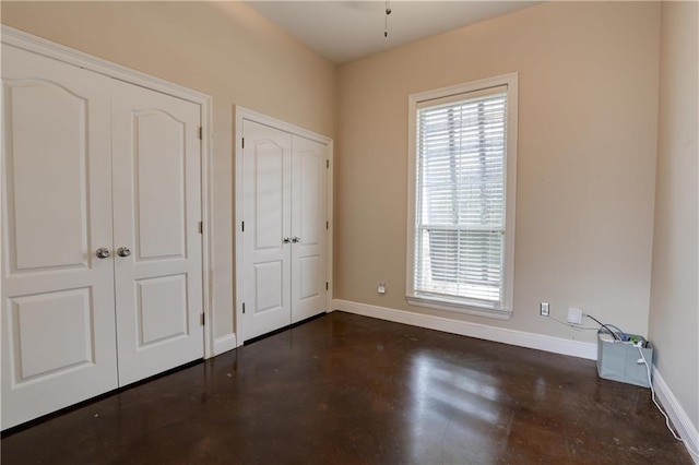 unfurnished bedroom with multiple closets, baseboards, and finished concrete floors