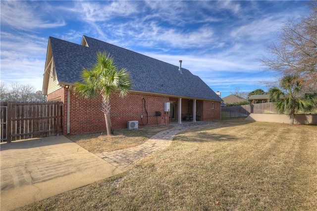 back of property with a yard, brick siding, a fenced backyard, and a shingled roof