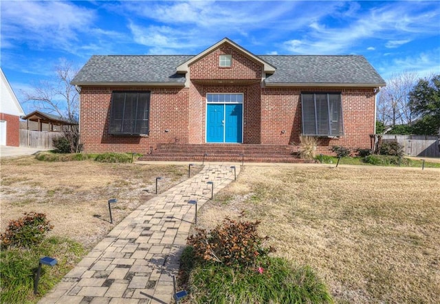 ranch-style home featuring brick siding, roof with shingles, and fence