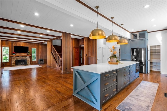 kitchen featuring hanging light fixtures, dark hardwood / wood-style floors, stainless steel fridge, and wooden walls