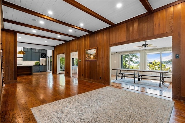 unfurnished living room with beam ceiling, wood walls, and dark hardwood / wood-style floors