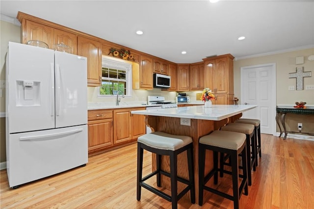 kitchen featuring light wood-type flooring, ornamental molding, white appliances, a center island, and a breakfast bar area