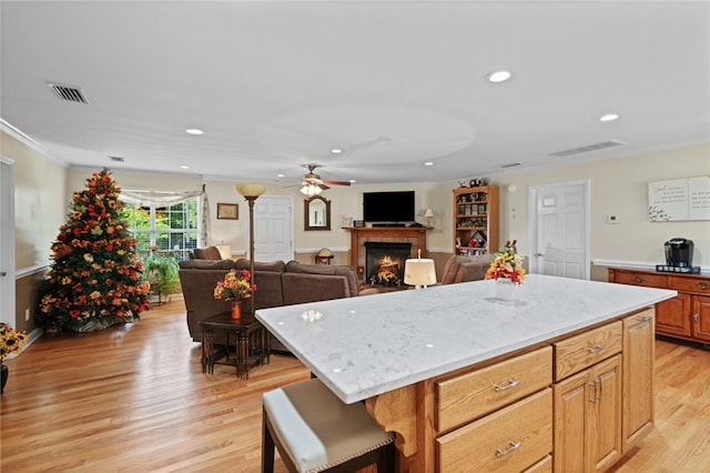 kitchen with a kitchen breakfast bar, light stone countertops, a center island, ceiling fan, and light wood-type flooring