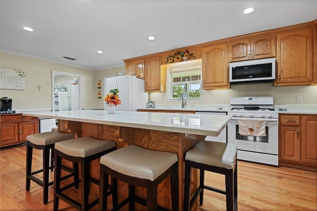 kitchen featuring crown molding, white appliances, light hardwood / wood-style flooring, a kitchen breakfast bar, and a center island