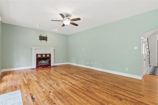 unfurnished living room with ceiling fan, a tile fireplace, and light hardwood / wood-style floors