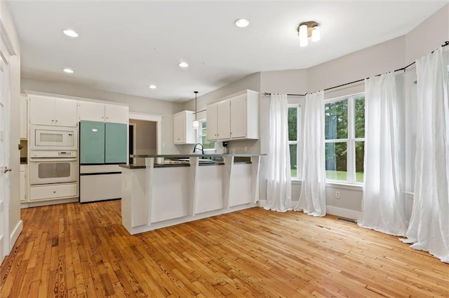 kitchen with white cabinetry, built in appliances, decorative light fixtures, kitchen peninsula, and light hardwood / wood-style floors