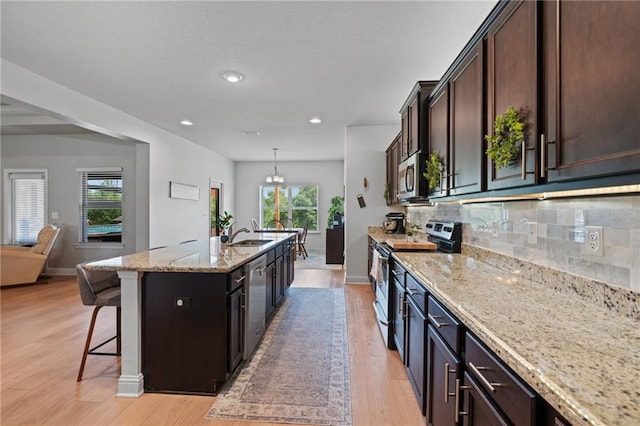 13077 Tara Point Dr, Mobile, AL 36695 - kitchen featuring appliances with stainless steel finishes, a breakfast bar area, light stone counters, light wood finished floors, and decorative backsplash