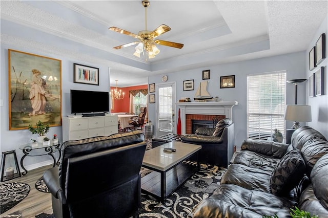 living room featuring a fireplace, ceiling fan with notable chandelier, ornamental molding, a raised ceiling, and hardwood / wood-style flooring