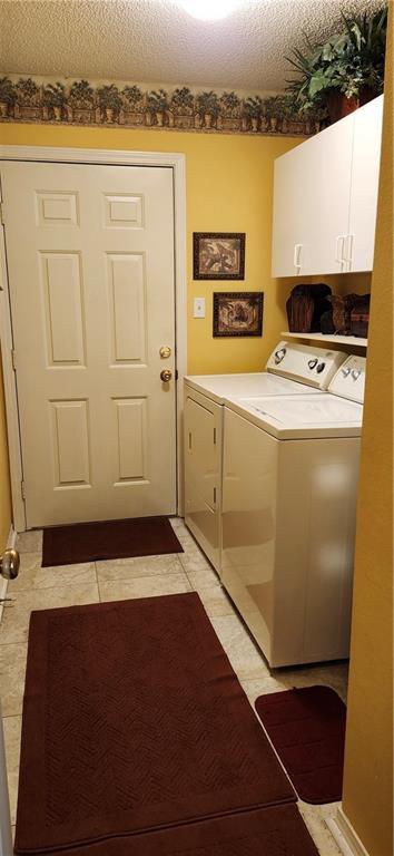 laundry room with washer and clothes dryer, light tile patterned floors, cabinets, and a textured ceiling