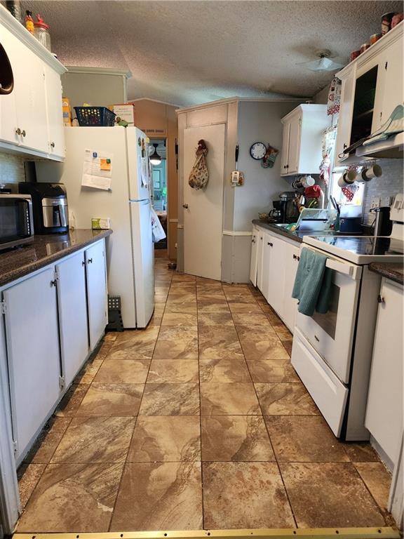 8560 Sadie Ct, Grand Bay, AL 36541 - kitchen with white appliances, dark countertops, white cabinets, a textured ceiling, and under cabinet range hood