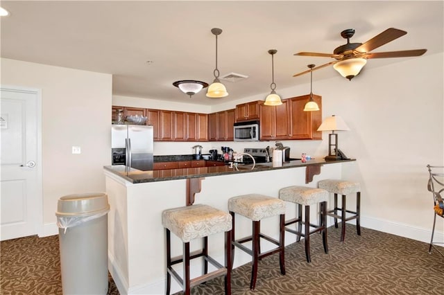 kitchen with appliances with stainless steel finishes, ceiling fan, kitchen peninsula, pendant lighting, and a kitchen bar