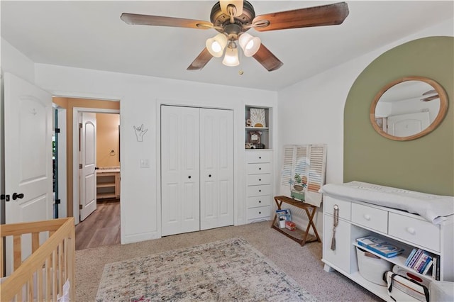 carpeted bedroom featuring ceiling fan, a nursery area, and a closet