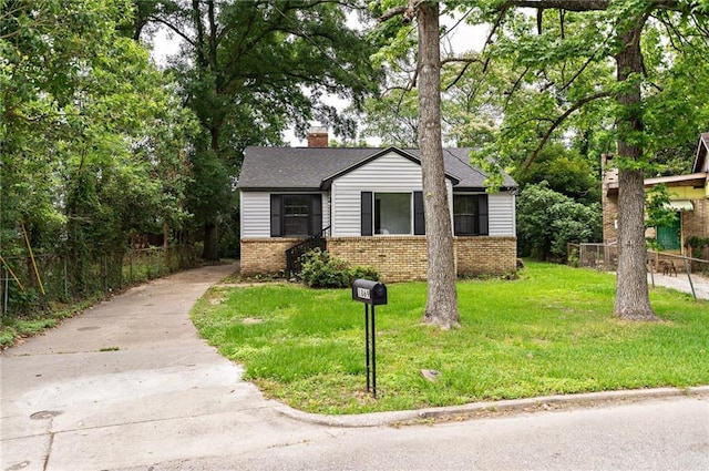 view of front facade with a chimney, brick siding, fence, and a front lawn