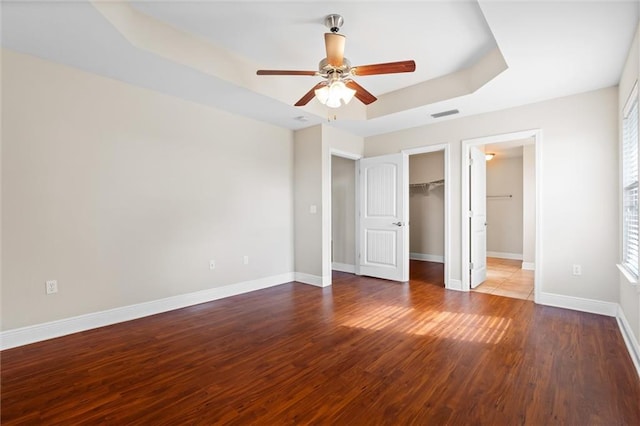 unfurnished bedroom featuring a walk in closet, a raised ceiling, ceiling fan, hardwood / wood-style floors, and a closet