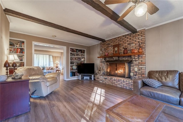 living room featuring a brick fireplace, built in shelves, wood-type flooring, crown molding, and beamed ceiling