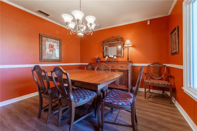 dining room with wood-type flooring, ornamental molding, and an inviting chandelier