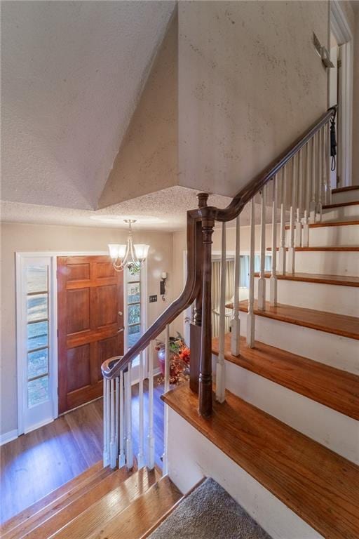 staircase featuring hardwood / wood-style floors, an inviting chandelier, and vaulted ceiling