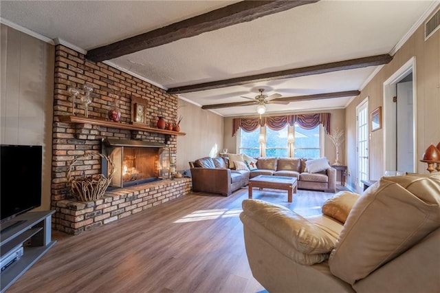 living room with hardwood / wood-style floors, ceiling fan, ornamental molding, a brick fireplace, and beam ceiling