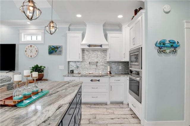 kitchen featuring stainless steel appliances, white cabinetry, light stone countertops, and custom range hood