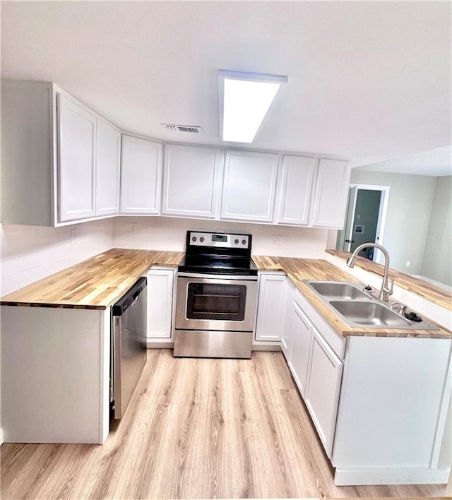 kitchen with appliances with stainless steel finishes, sink, wood counters, white cabinetry, and light hardwood / wood-style flooring